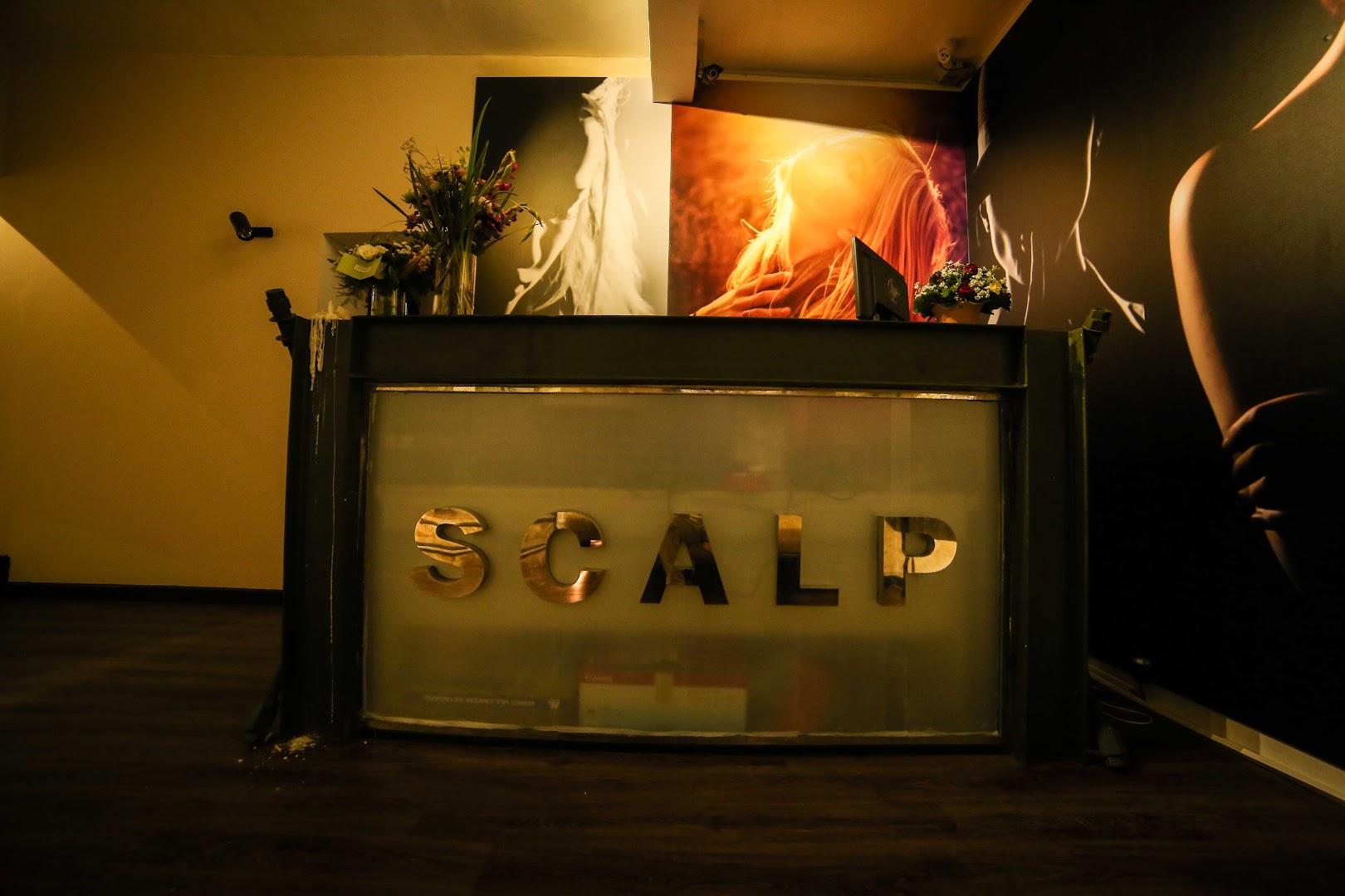 Scalp reception desk with large gold lettering and hair portrait murals